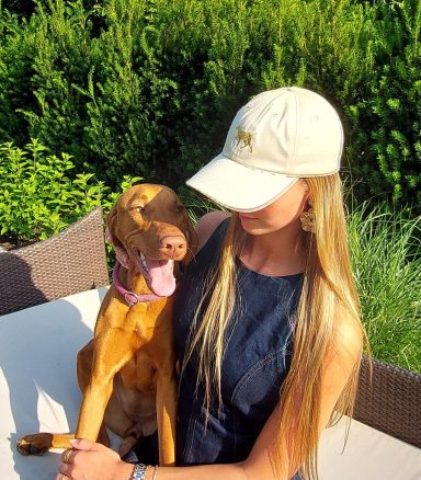 Junge Frau mit einer blonden langen Haartracht und Hund sitzt in einem Garten.